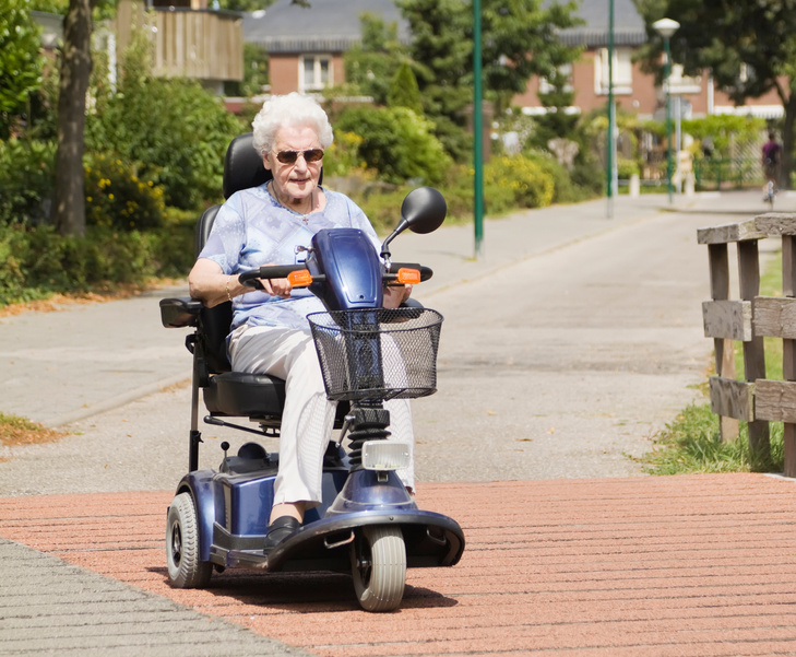 Elderly woman driving mobility scooter down quiet street